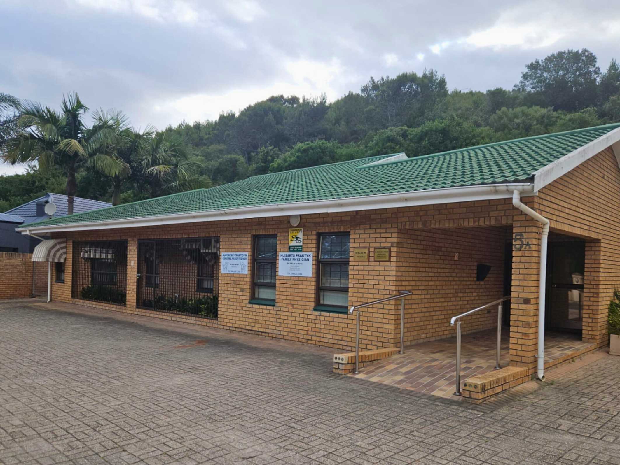 Single-story brick building with a green tiled roof, ramp access, and signs indicating a general practitioner and family physician office.